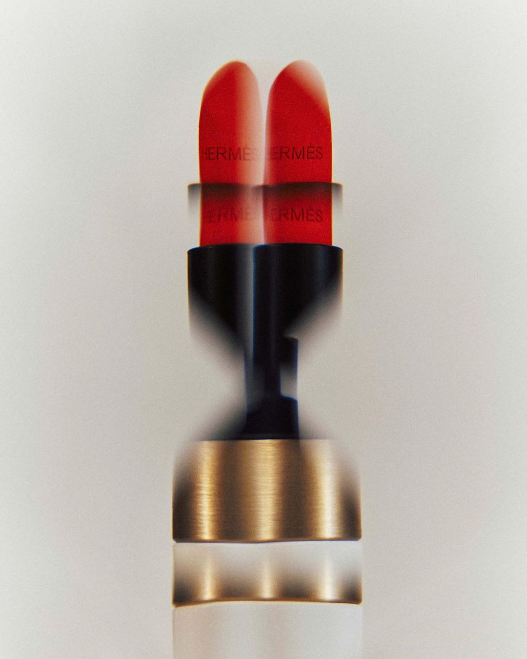 Close-up studio shot of red Hermès lipstick with black and gold casing, showing motion blur against a clean white background.