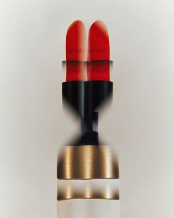 Close-up studio shot of red Hermès lipstick with black and gold casing, showing motion blur against a clean white background.
