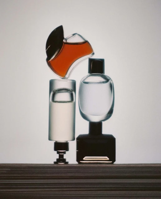 Still life shot of three perfume bottles of varying shapes, sizes, and colors placed on a multi-layered wooden surface, creating visual contrast.