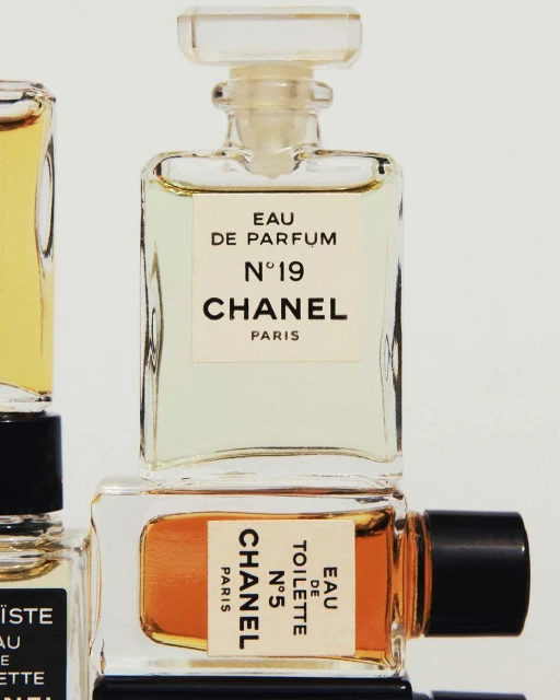 Close-up studio shot of Chanel N°5 and N°19 Eau de Parfum bottles with clear glass, white labels, and golden and amber liquid tones.
