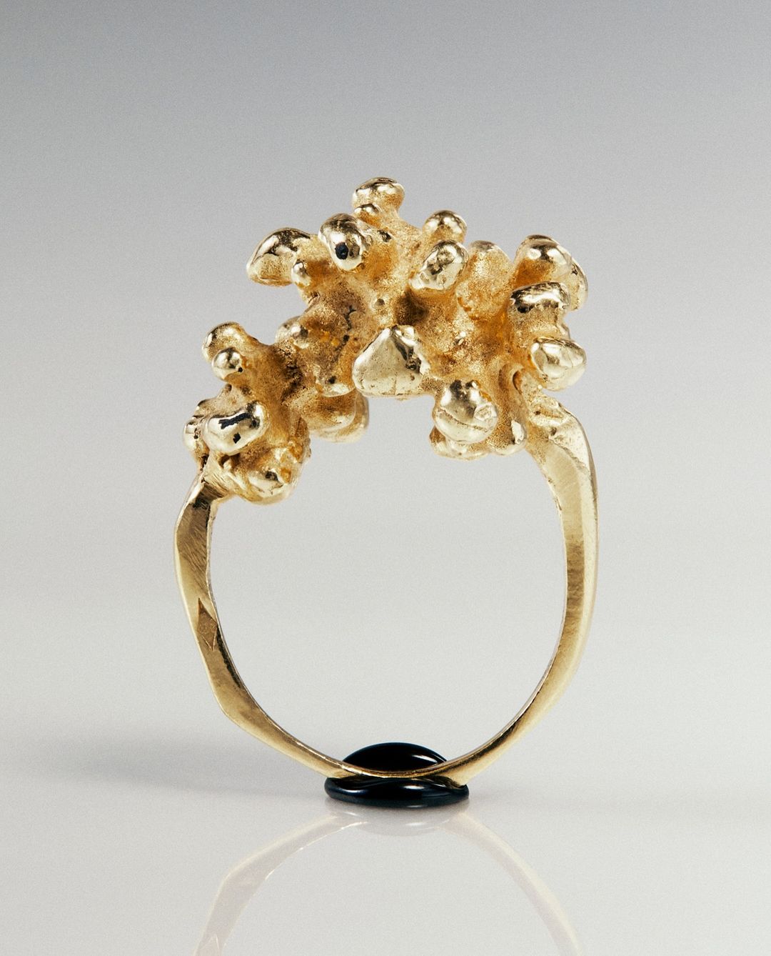 Close-up of an ornate gold ring with a textured, branch-like design, set against a soft, neutral background highlighting its intricate details.
