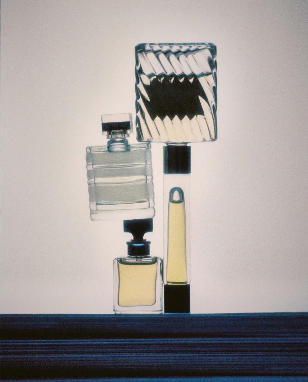 Still life arrangement of four clear glass perfume bottles with dark caps against a neutral background, showcasing various shapes and designs.