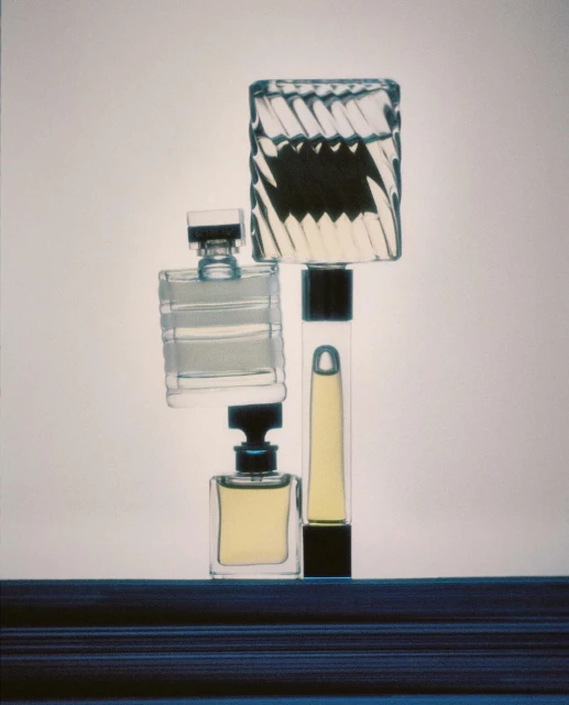 Still life arrangement of four clear glass perfume bottles with dark caps against a neutral background, showcasing various shapes and designs.