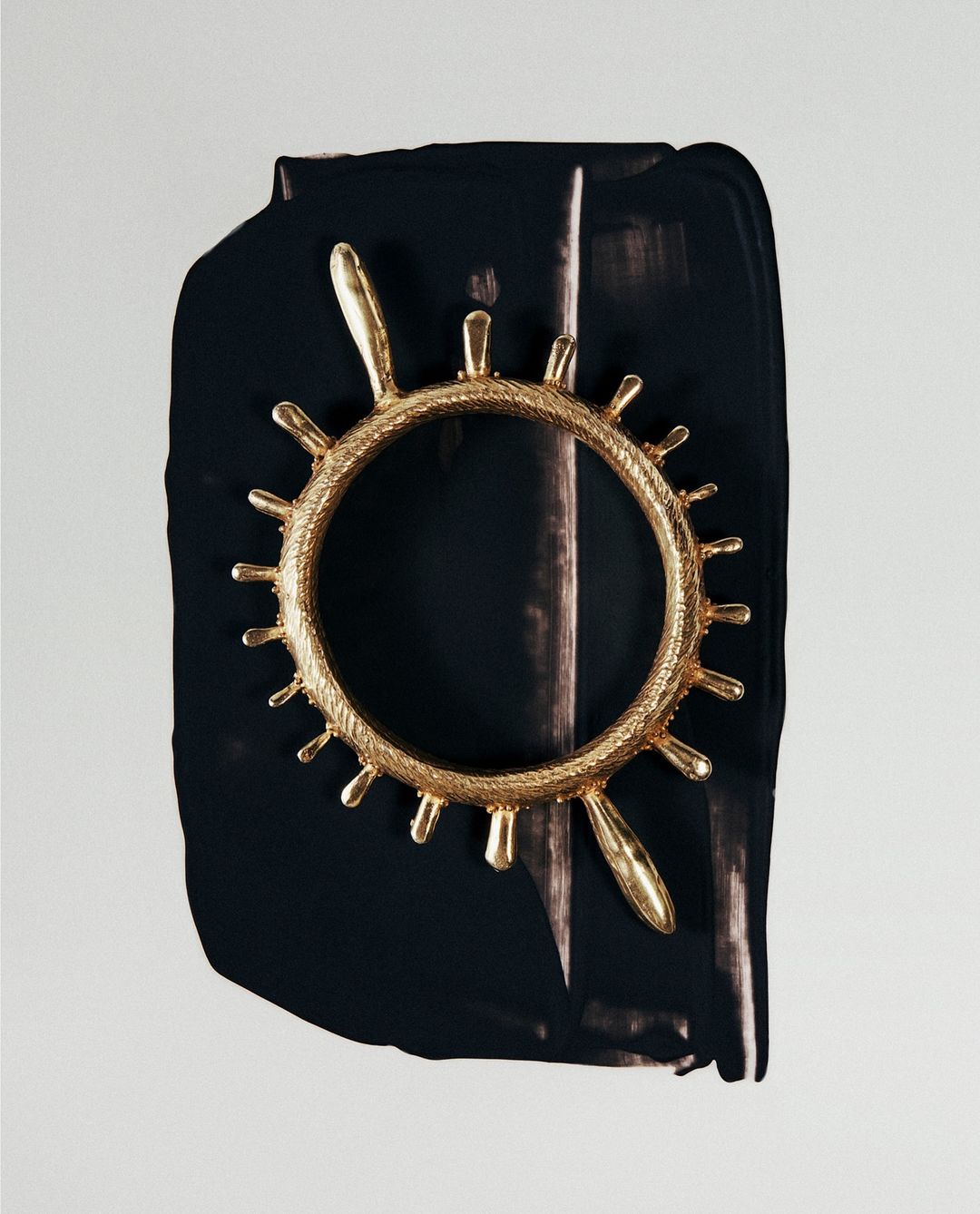 Abstract close-up of a gold ornamental ring against a black and white painted backdrop, showcasing texture and contrasting colors.