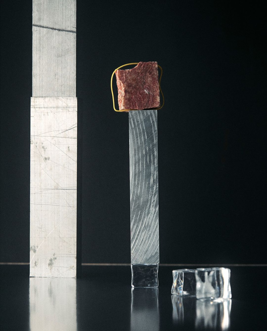 Abstract still life photography of a red rock secured with a gold wire on a textured glass post with a black background.