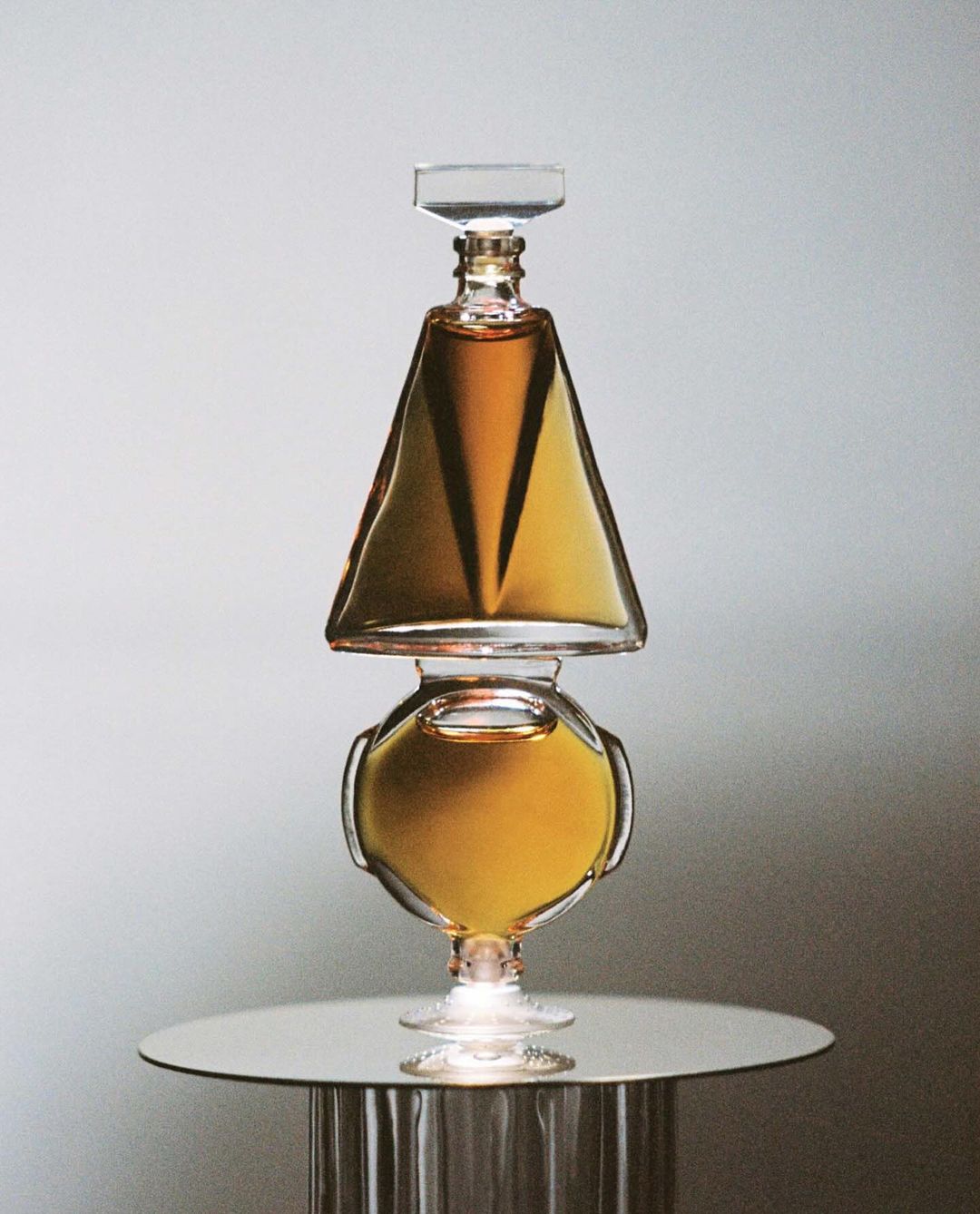 Elegant still life of stacked glass decanters filled with amber liquid, set on a reflective table against a gradient grey backdrop.