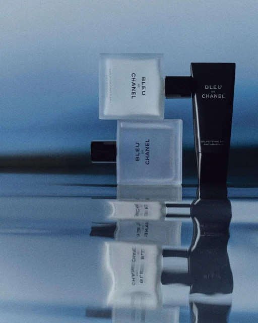 Bleu de Chanel product presentation on reflective surface. Includes perfume bottle, body wash and aftershave lotion against blue background.