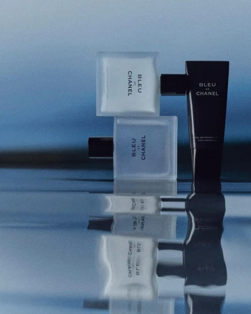 Bleu de Chanel product presentation on reflective surface. Includes perfume bottle, body wash and aftershave lotion against blue background.