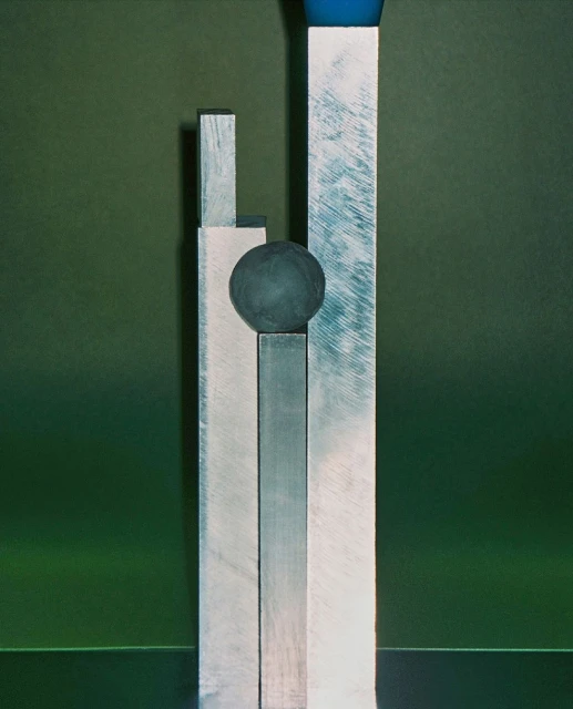 Abstract composition featuring a dark orb atop a stack of brushed silver bars against a contrasting green backdrop.