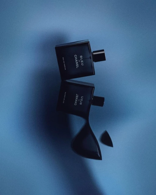 Two Chanel Bleu de Chanel bottles, one upright and one reflected, on a bright blue surface, showcasing a men's fragrance product shot.