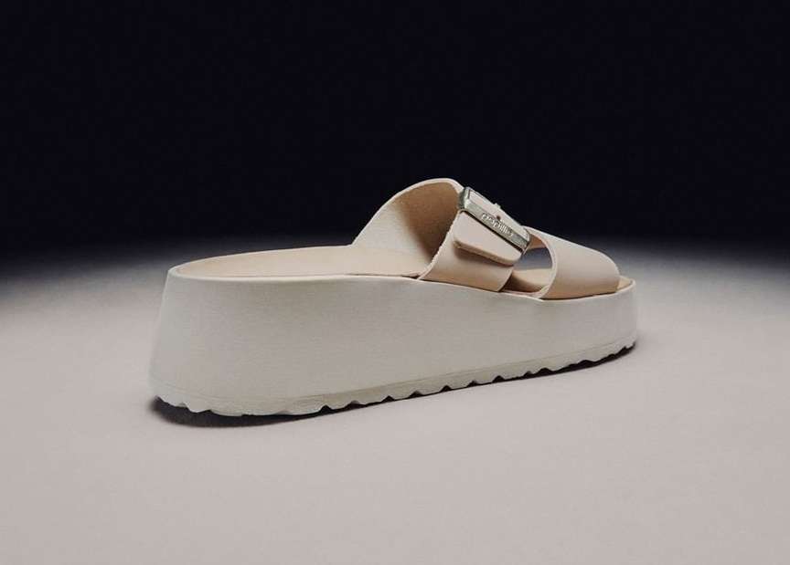 Platform slide sandal on white surface against dark gray backdrop. Close-up of the fashionable, modern sandal with silver hardware.