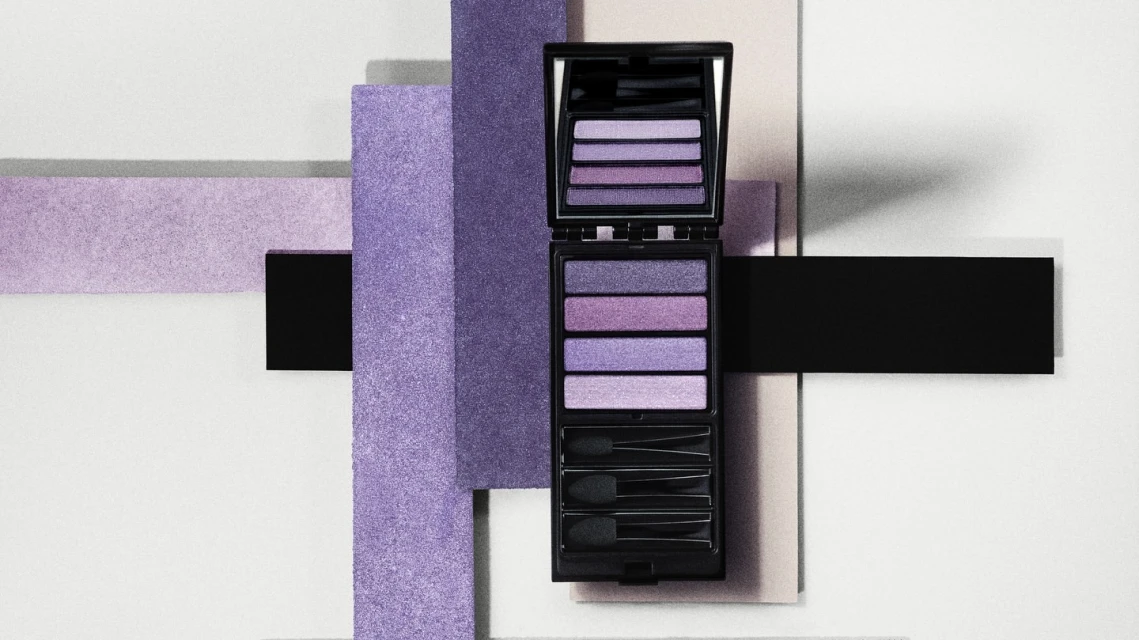 Eye shadow palette in black case with mirror surrounded by purple and black geometric shapes on white surface, cosmetic product.