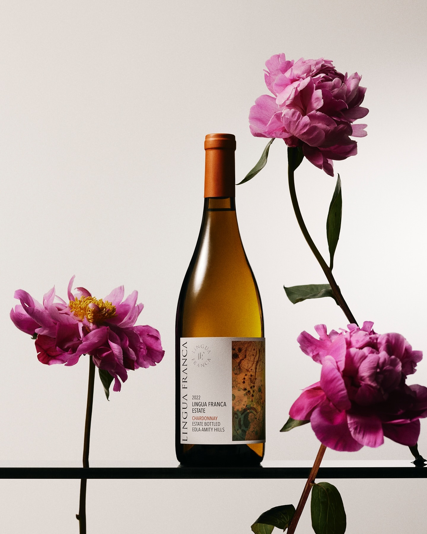 Elegant still life of a white wine bottle, 'Lingua Franca,' accented by vibrant pink peonies against a soft, neutral background.