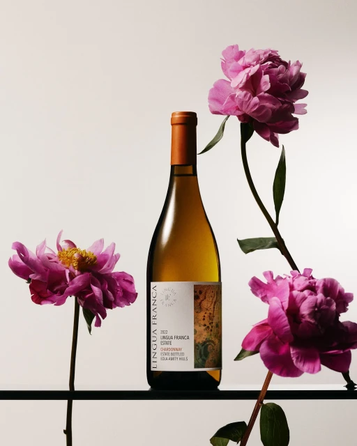 Elegant still life of a white wine bottle, 'Lingua Franca,' accented by vibrant pink peonies against a soft, neutral background.