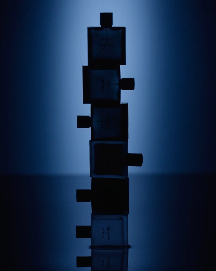Stack of Bleu de Chanel fragrance bottles against a blurred blue gradient backdrop, highlighting the product's design and color palette.