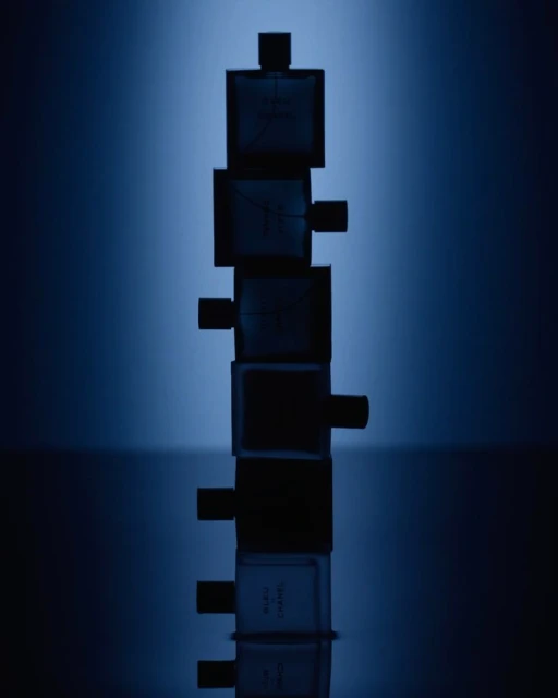 Stack of Bleu de Chanel fragrance bottles against a blurred blue gradient backdrop, highlighting the product's design and color palette.