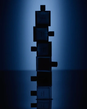 Stack of Bleu de Chanel fragrance bottles against a blurred blue gradient backdrop, highlighting the product's design and color palette.