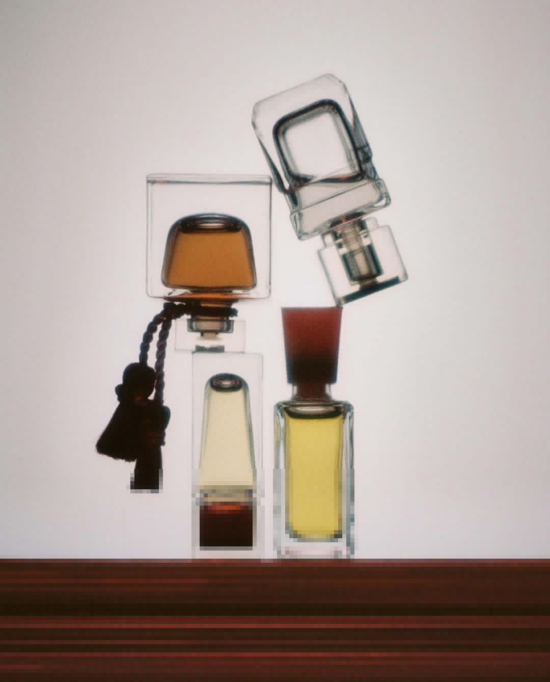 Four perfume bottles of various shapes and sizes sit atop a dark wood surface against a pale gradient backdrop, creating a clean aesthetic.
