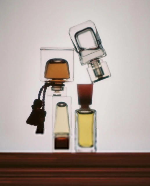 Four perfume bottles of various shapes and sizes sit atop a dark wood surface against a pale gradient backdrop, creating a clean aesthetic.