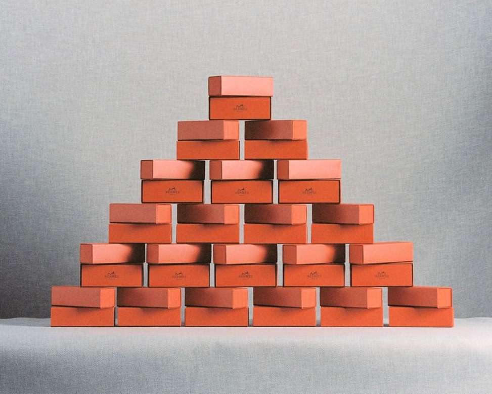 Pyramid of orange and peach-colored boxes with lids stacked against a gray background, creating a simple yet elegant studio shot.
