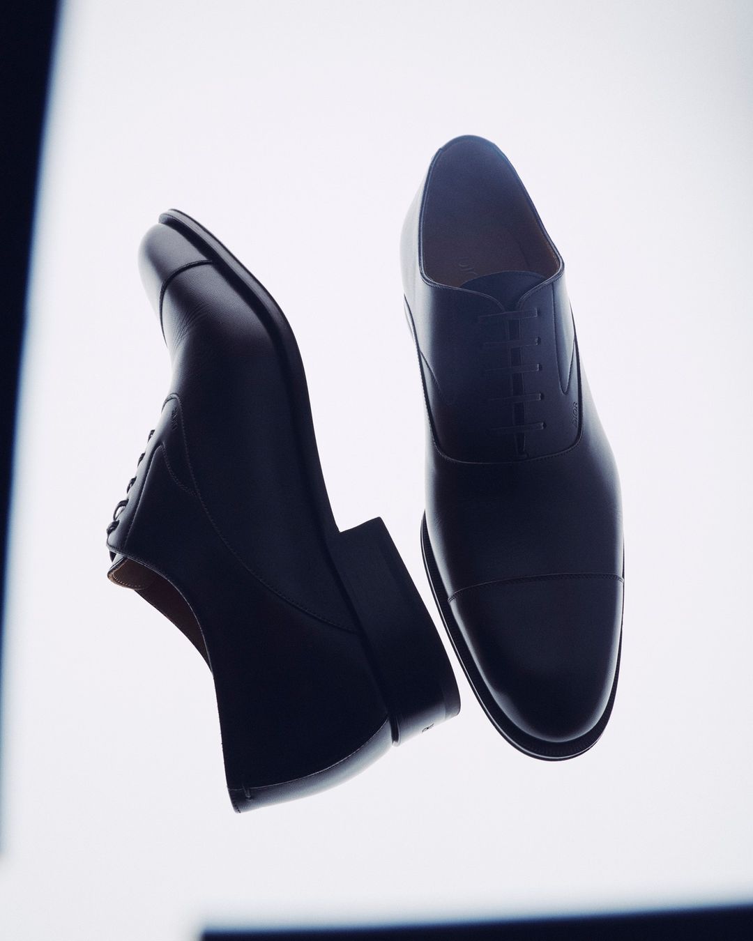 Close-up studio shot of pair of black leather Oxford dress shoes on white background with diffused lighting and formal menswear feel.