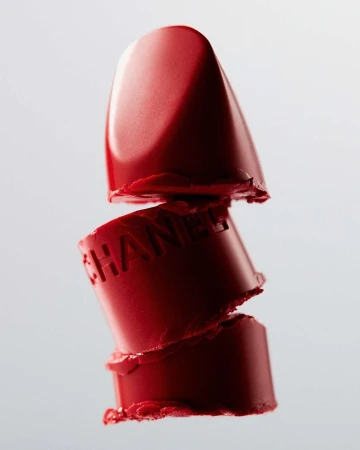 Extreme macro close-up of a stacked, severed red lipstick tube with embossed lettering against a pale grey background.
