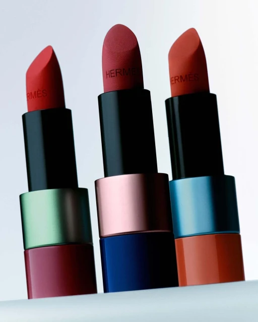 Three red-toned Hermes lipsticks in a row showcase beauty product photography, highlighting luxury cosmetic details on a light background.