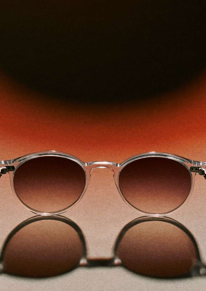 Studio shot of round-framed sunglasses with brown gradient lenses reflected against a warm-toned background, emphasizing product photography.