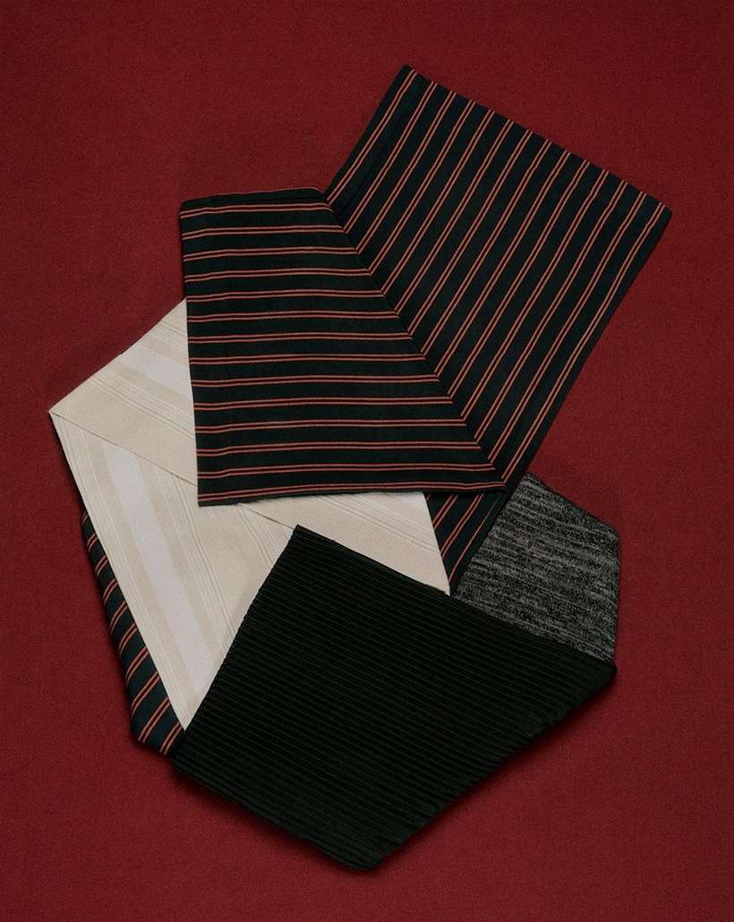 Abstract textiles composition on a red surface, featuring striped, ribbed, and patterned fabrics arranged in a geometric design.