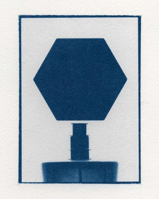 Abstract cyanotype image of a geometric, three-tiered, symmetrical object against a white background within a dark blue border.