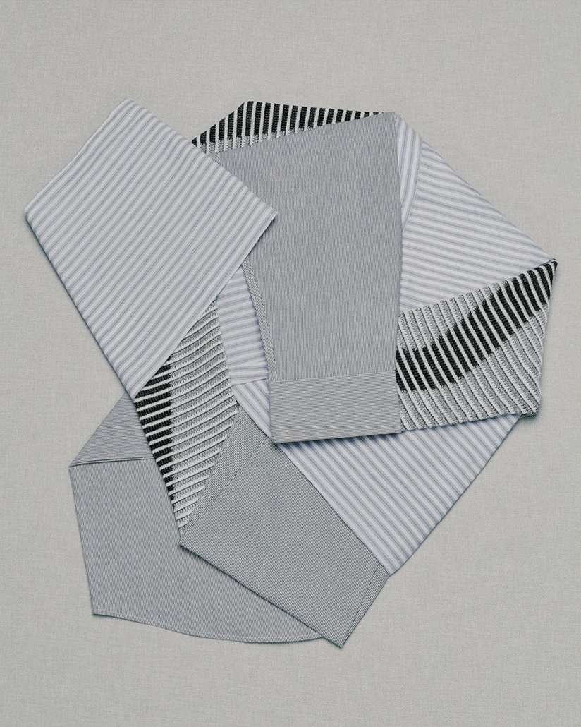 Still life shot of folded blue and white striped shirts on a light gray surface, creating a geometric composition.