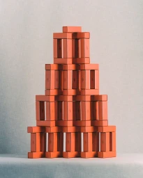 A symmetrical pyramid structure built from stacked rectangular orange boxes against a textured neutral background