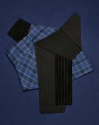Folded blue plaid shirt and dark pinstripe trousers arranged on a textured blue fabric surface.