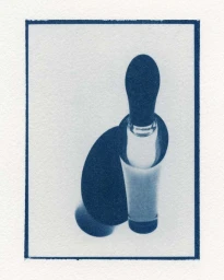 Cyanotype photographic print featuring a vertical bottle casting a dark oval shadow on textured paper