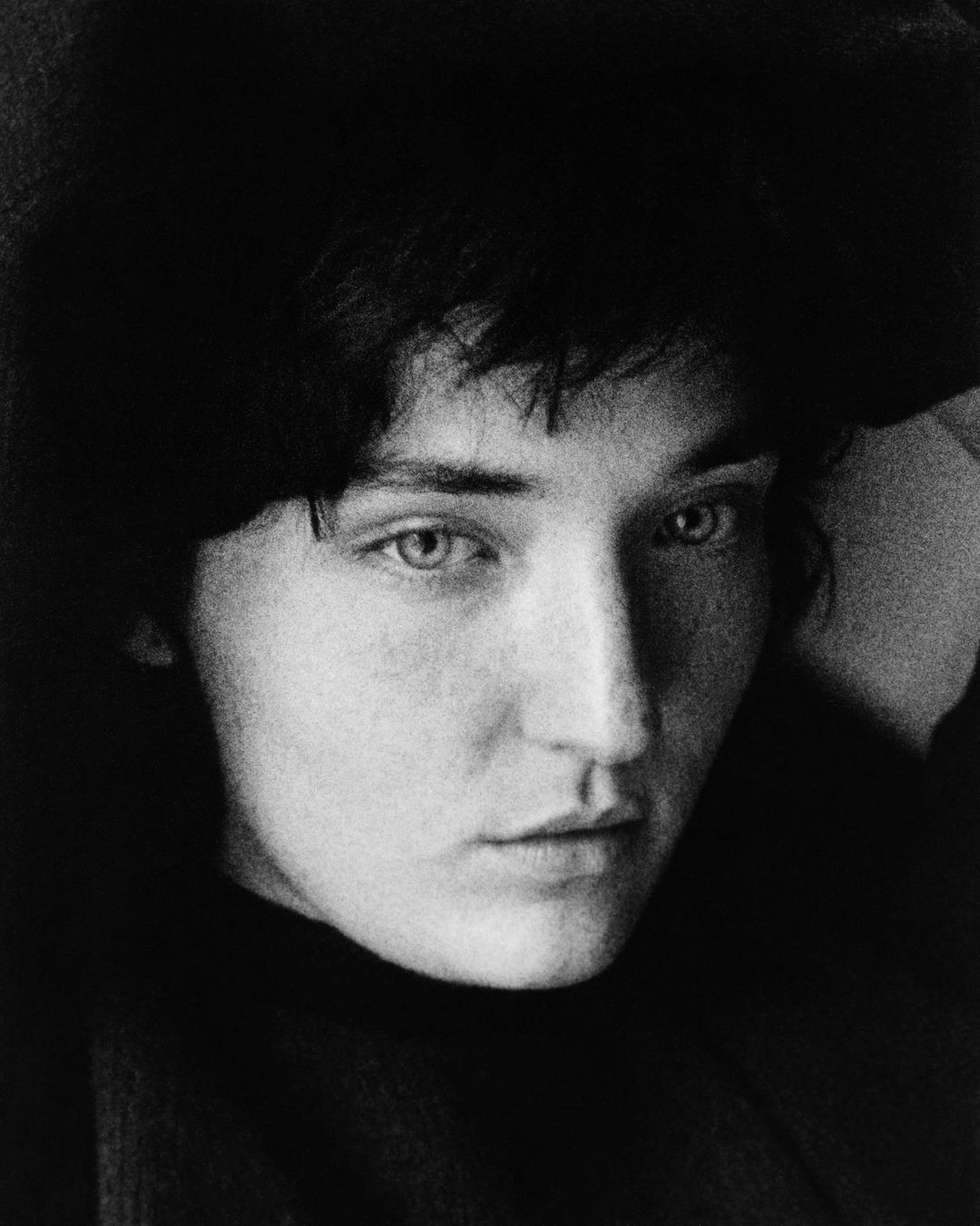 Monochrome portrait of a dark-haired adult female with light eyes, gazing intently at the camera in a simple studio setting.