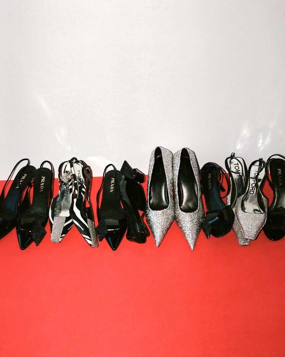 Display of luxury high heels including brands such as Prada and Tom Ford in black, zebra print and silver on a red and white background.
