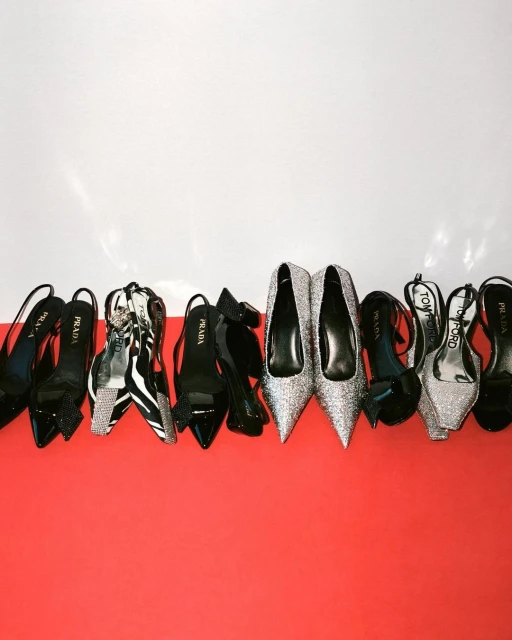Display of luxury high heels including brands such as Prada and Tom Ford in black, zebra print and silver on a red and white background.