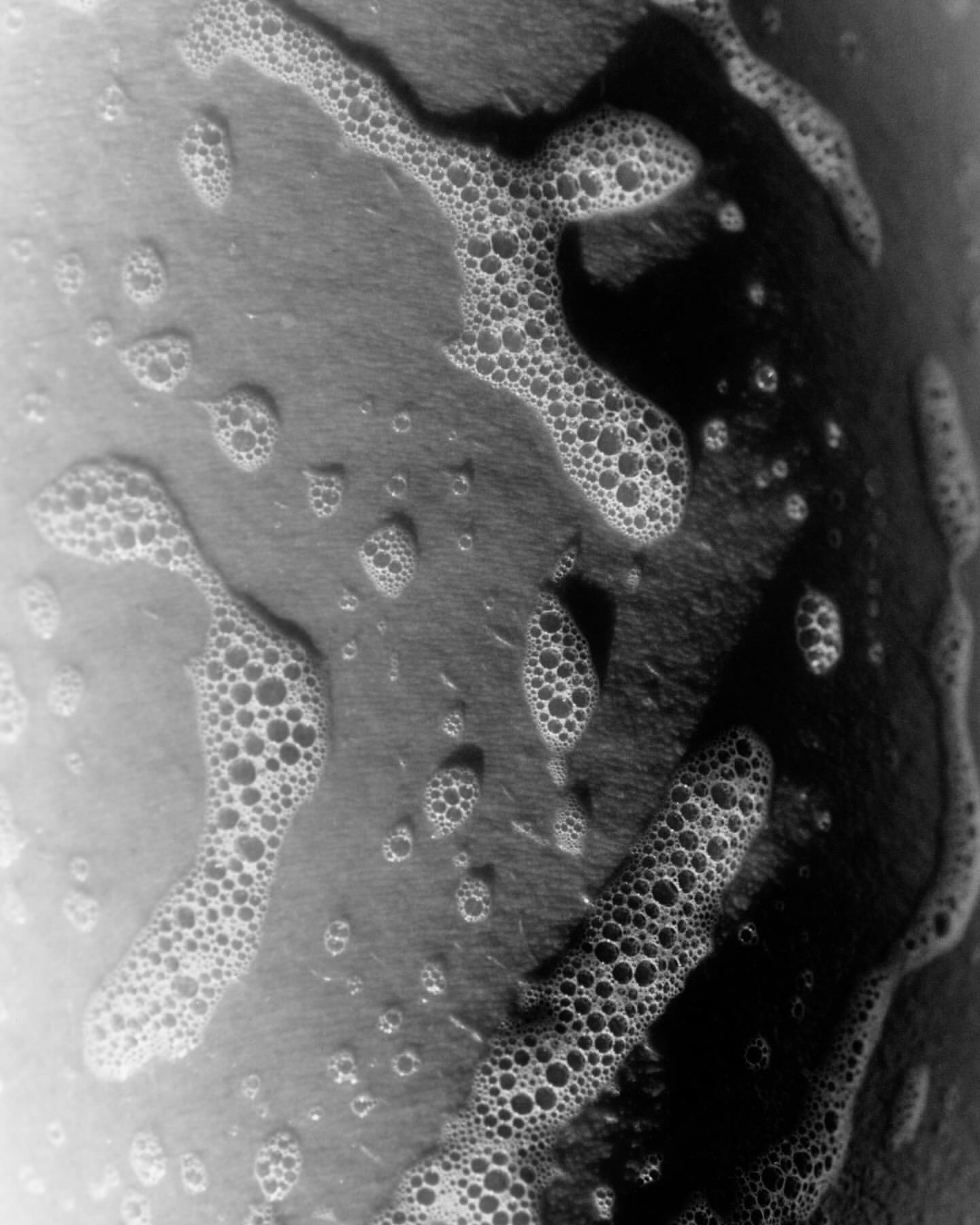 Close-up of soap bubbles on a surface in black and white, creating an abstract and textured visual pattern.