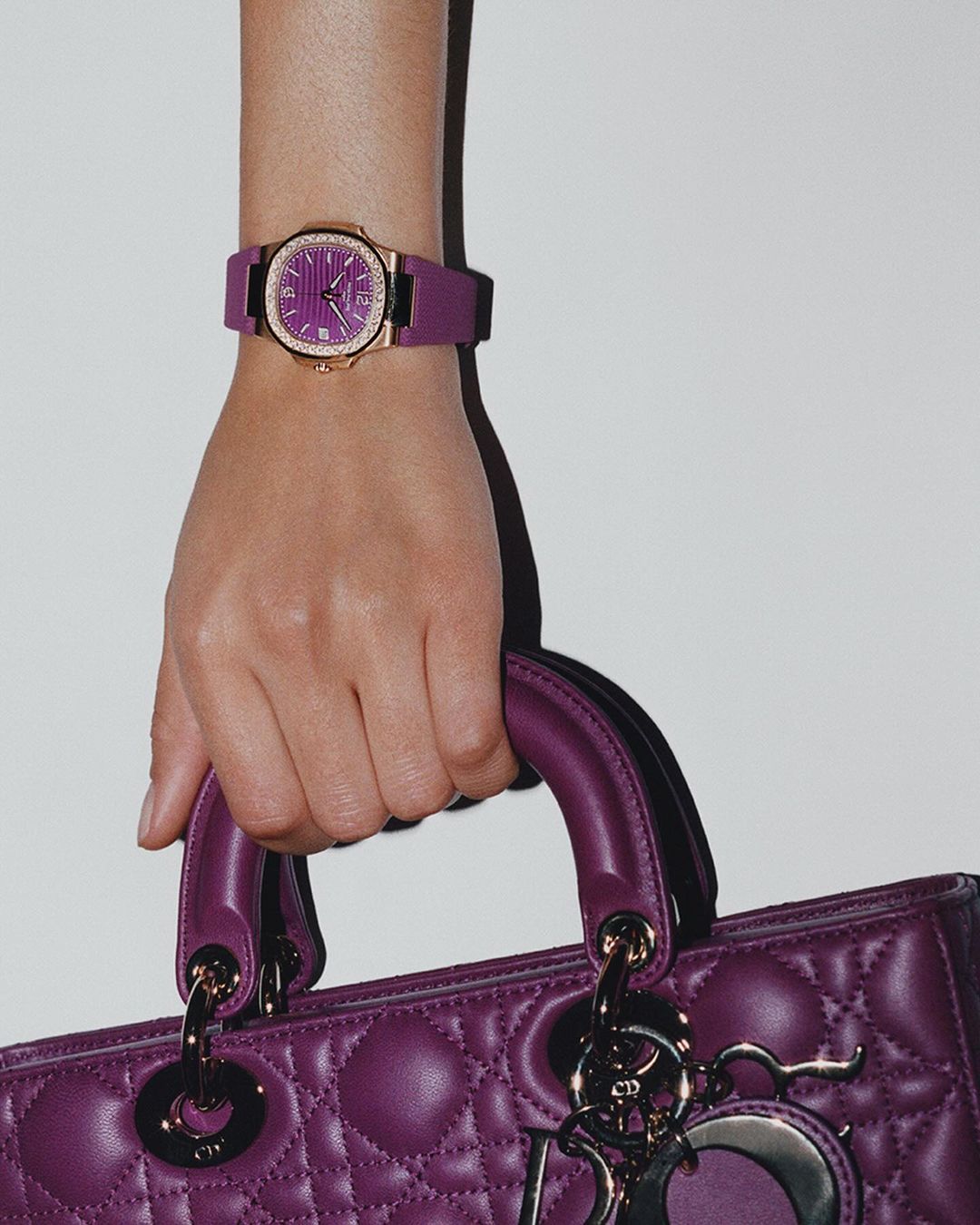 Close-up of a woman's hand holding a purple leather purse, showcasing a stylish wristwatch with a gold case and purple band.