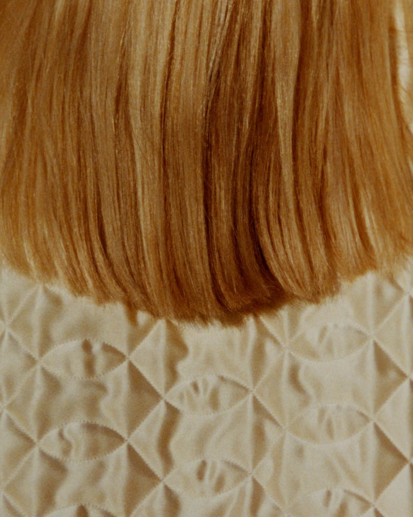 Close-up shot of textured beige fabric beneath strands of blonde hair. Neutral color palette and soft lighting.