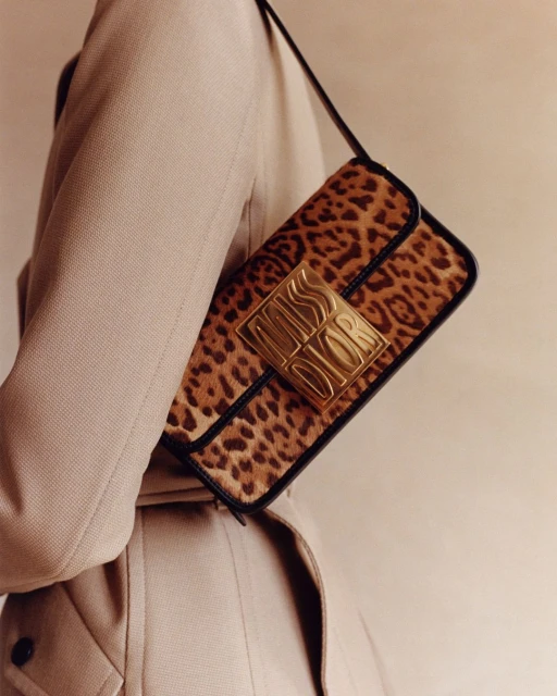 Leopard print Miss Dior handbag with gold hardware. Shoulder bag with animal print and gold logo, accessorized with beige trench coat.