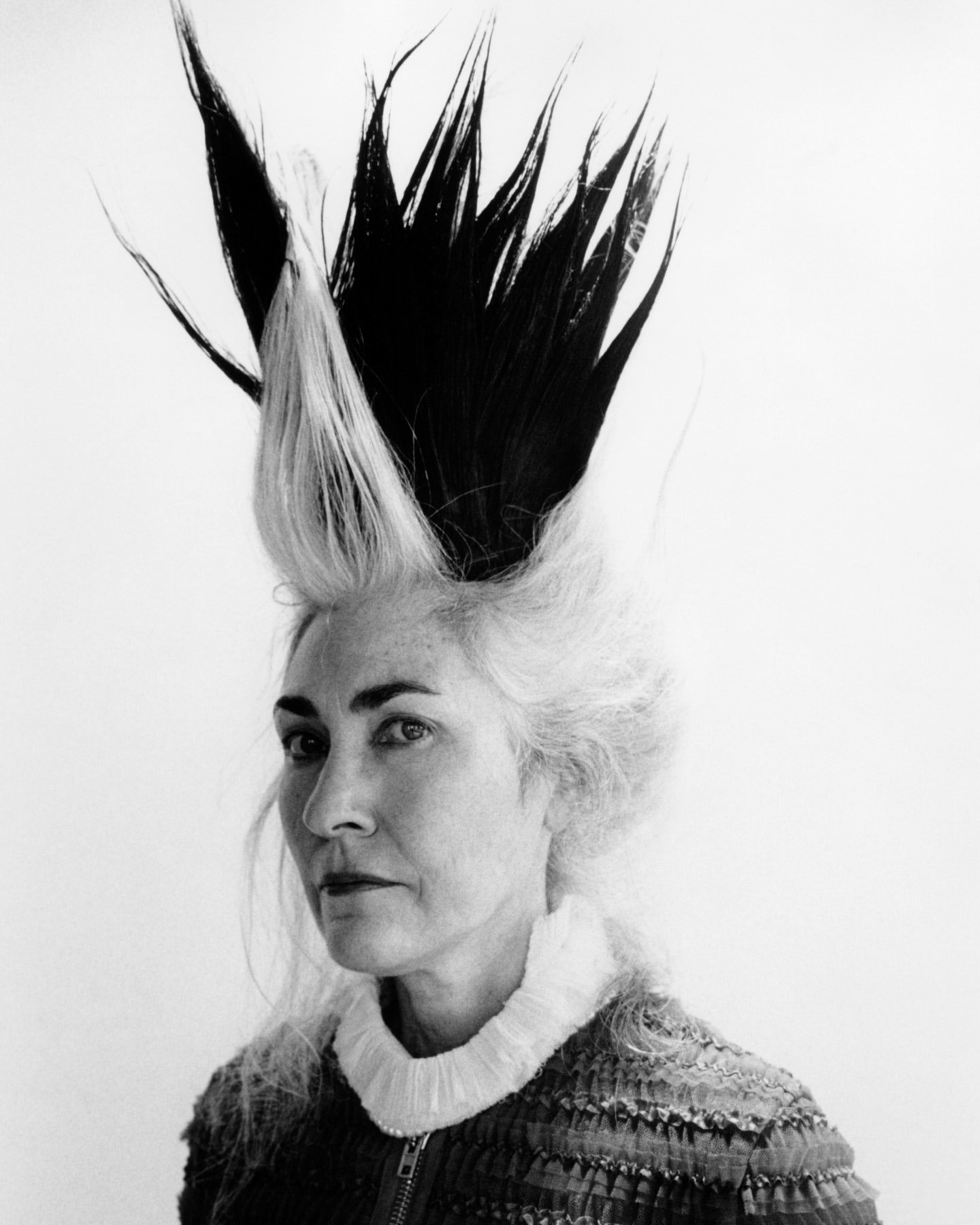 Striking black and white portrait of a woman with avant-garde black and white hair standing against a stark white background.