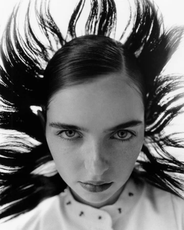 Close-up portrait of a young woman with dark hair styled upwards, creating a dynamic, eye-catching frame around her face in monochrome.