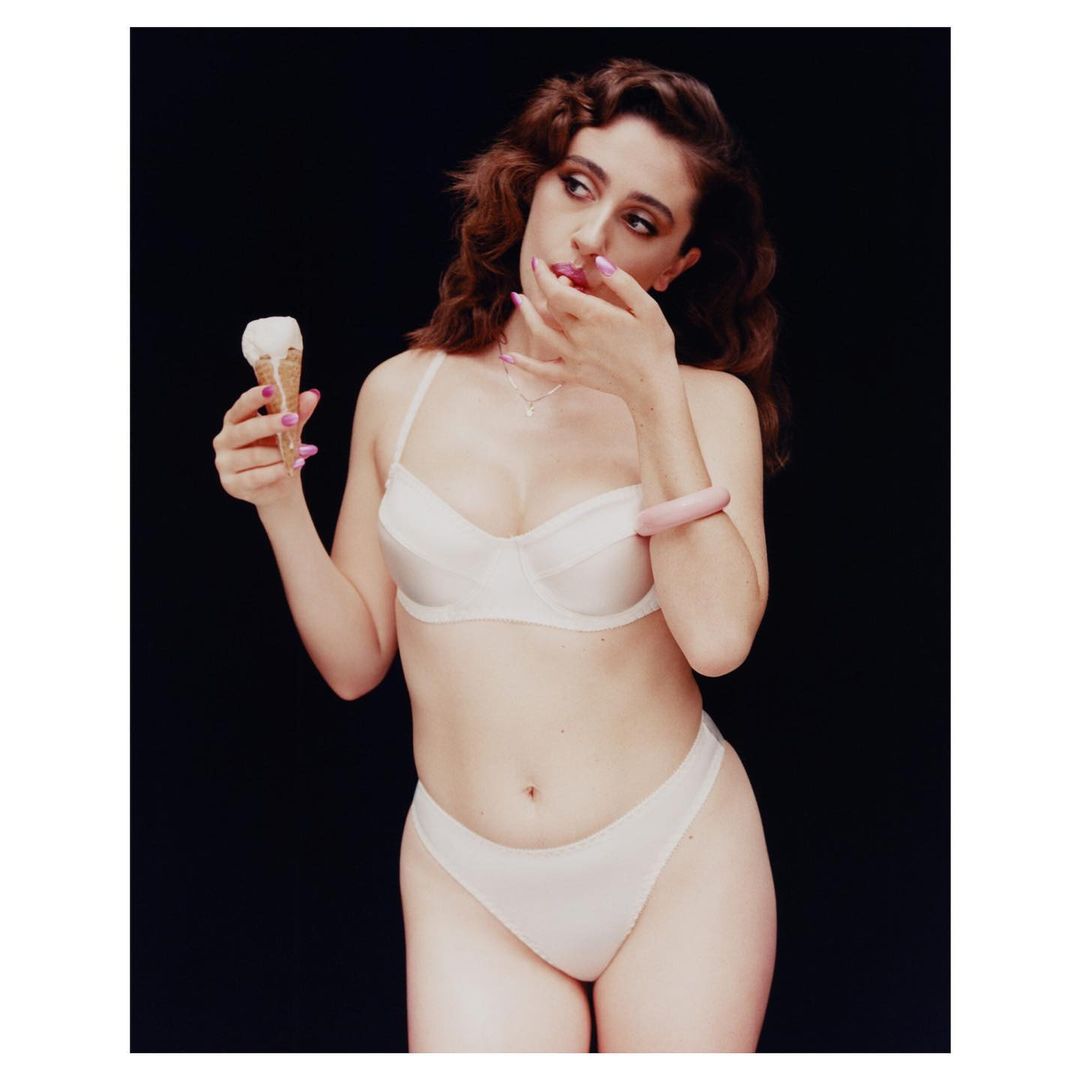 Woman in lingerie holding an ice cream cone against a dark background in a studio setting, showing her waist-up.