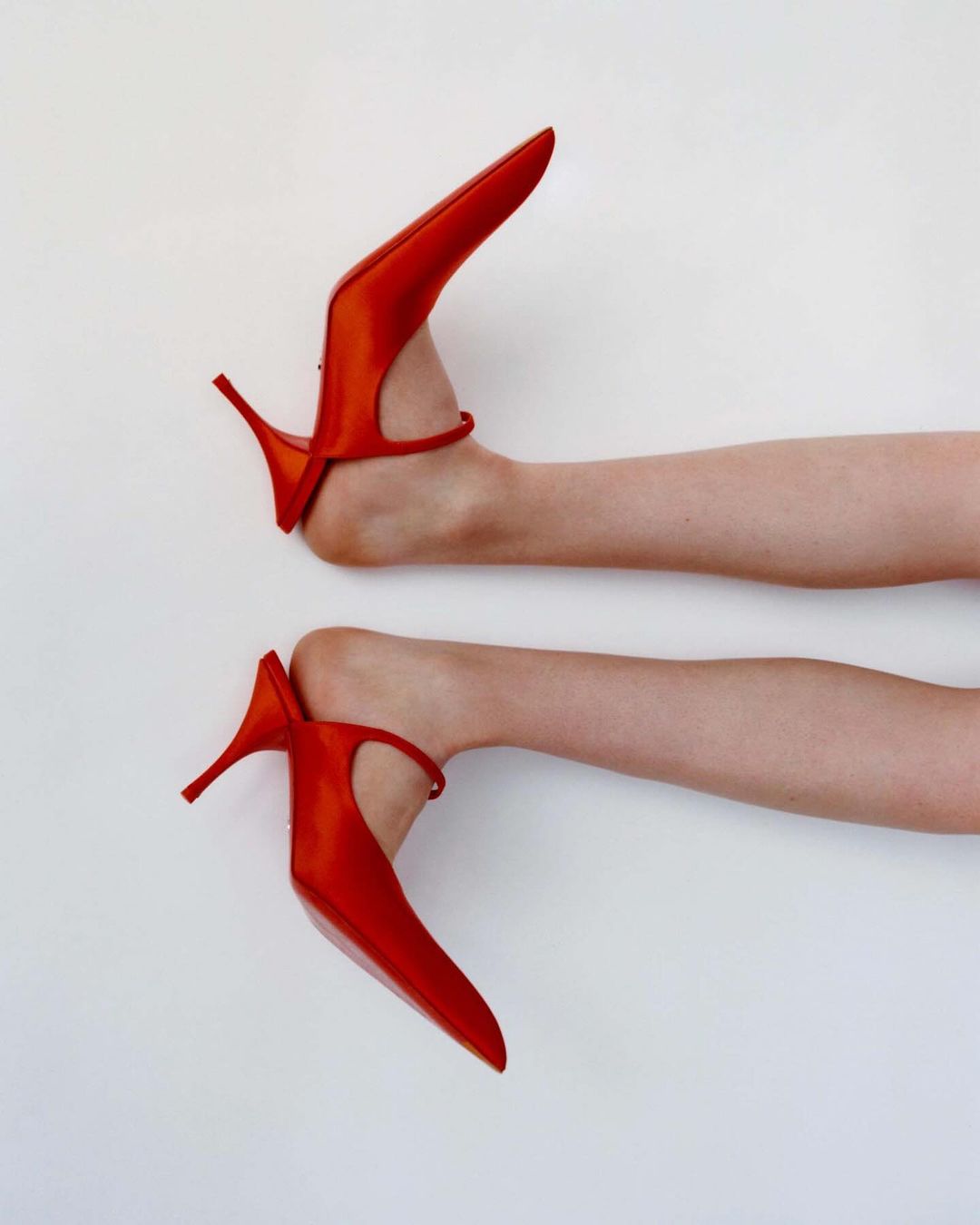Close-up shot of two bare feet wearing bright red high-heeled shoes against a plain white background.