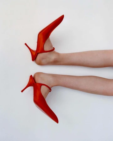 Close-up shot of two bare feet wearing bright red high-heeled shoes against a plain white background.