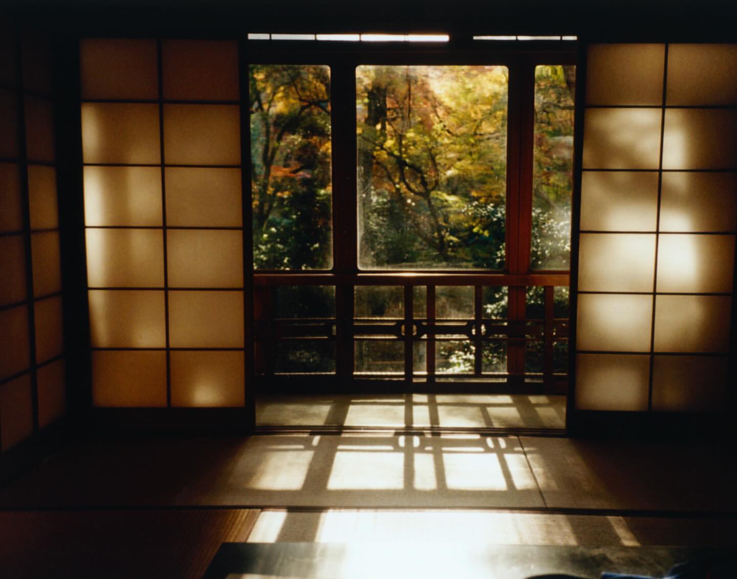 Interior view of traditional Japanese room with shoji screens and wood windows overlooking an autumn garden with colorful trees.