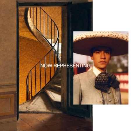 Portrait of a young adult in traditional Mexican attire with a wide brim sombrero, set against a backdrop of a spiral staircase.