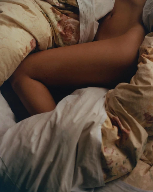 Human form nestled in patterned bedding with light skin tone, creating a cozy and intimate visual experience in the bedroom.