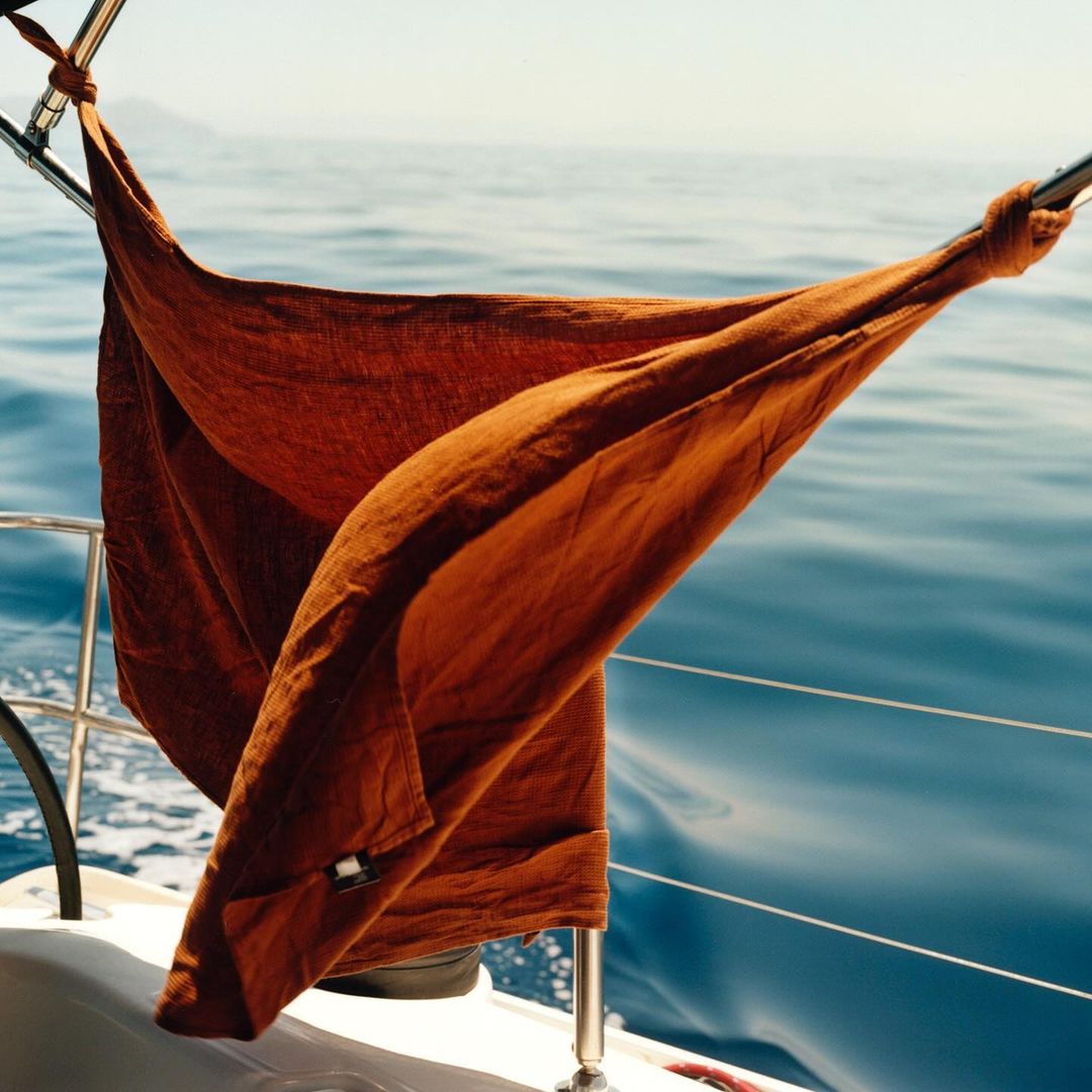 View of the ocean from a sailboat with a rust-colored towel drying on the railing under sunlight, creating a peaceful nautical scene.